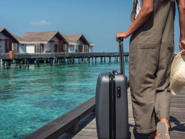 女性は熱帯の目的地で木製の桟橋にトロリーを引っ張ります - travel suitcase hawaiian shirt people traveling ストックフォトと画像