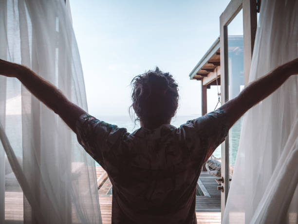 istock Man opening curtains in hotel room at sunrise 1301249309