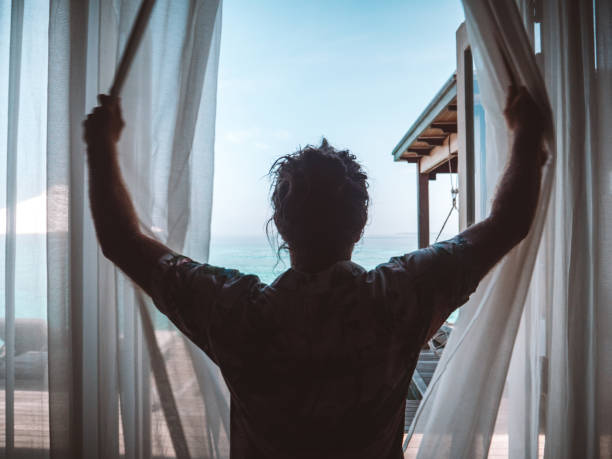 istock Man opening curtains in hotel room at sunrise 1301249369