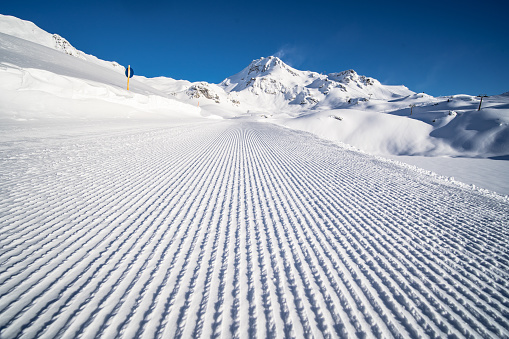 low angle view empty fresh groomed ski run on sunny winter day in snow covered european mountains with clear blue sky
