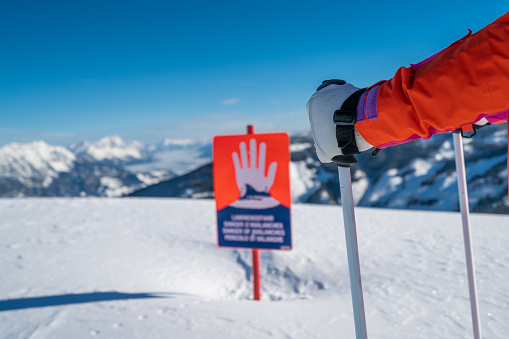 hand arm of one female skier standing stopping at danger of avalanche sign warning stop in deep snow high up in winter mountains on sunny day shallow focus on arm