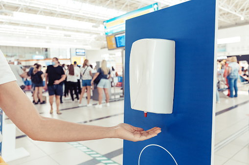 A female passenger disinfects her hands with an automatic sanitizer dispenser in the airport. Health care and protection from infection during the coronavirus pandemic