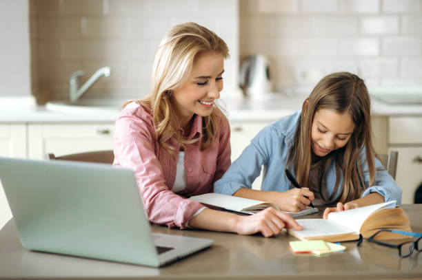istock Learning at home. Caring mom helps her beloved daughter do her homework, they sit at the table at home, using a laptop, books and a notebook. Homeschooling 1301251966