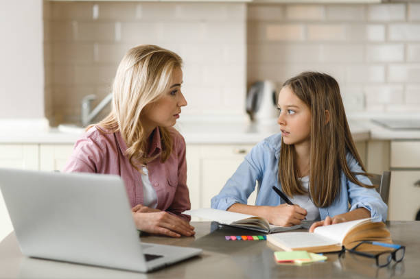 istock Distance learning. Mom helps her daughter do her homework, they sit at the table at home, using a laptop, books and a notebook. Homeschooling 1301251979