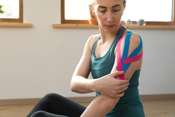 istock Young fit women checking her shoulder with elastic therapeutic kinetic tape. Performing exercise at home. Kinesiology physical therapy. 1301253270