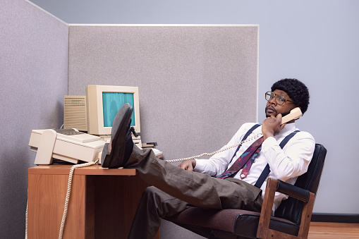 A vintage African American business man at the office works at an old computer at his cubicle desk.  1980's - 1990's fashion style.