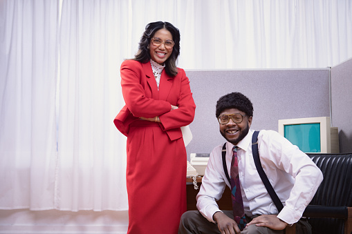 A vintage African American business man and a Filipino business woman at the office works at an old computer cubicle desk.  1980's - 1990's fashion style.