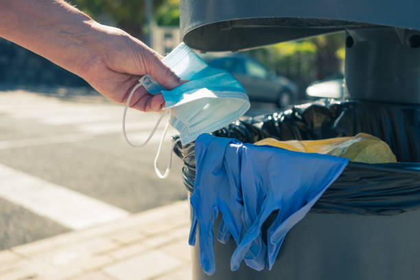 istock Human hand throws a surgical mask and protective gloves used to protect against the coronavirus into the garbage can in the city street 1301257768