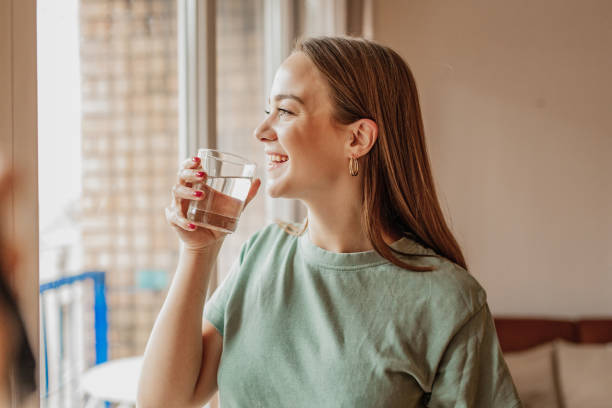 istock Young woman drinks water from a glass by the window 1301257917