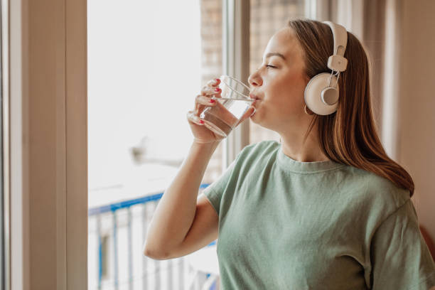istock Young woman drinks water from a glass by the window 1301257918