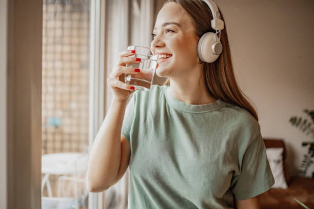 istock Young woman drinks water from a glass by the window 1301258223