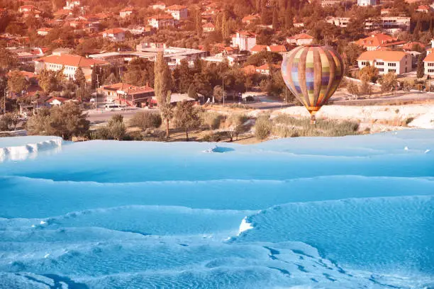 Photo of Hot Air balloon with tourists flying over the famous Turkish travel attraction - Pamukkale resort with thermal springs and limestone travertines