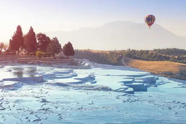 Photo of Hot Air balloon with tourists flying over the famous Turkish travel attraction - Pamukkale resort with thermal springs and limestone travertines