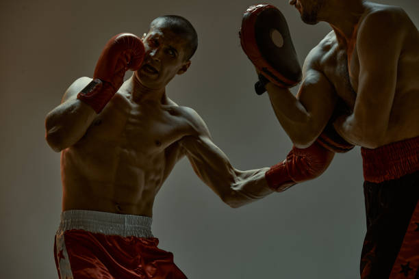 istock Fighting guys boxers during workout on gray studio background. Athletic males in boxing gloves training 1301268377