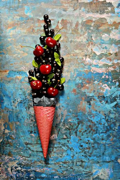 Ice cream in a waffle cup with black currant berries, ripe cherries and fresh mint leaves, copy space.Top view, flat lay. Fresh berries on a blue  background. Summer and healthy food concept.