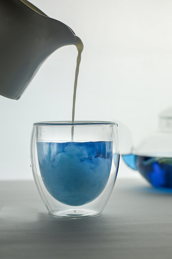 pouring milk in the blue butterfly tea in the grass cup, glass tea pot at the background. High quality photo