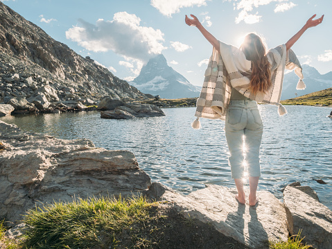She stands arms outstretched  on rock by the lake below the famous Matterhorn mountain peak . Switzerland