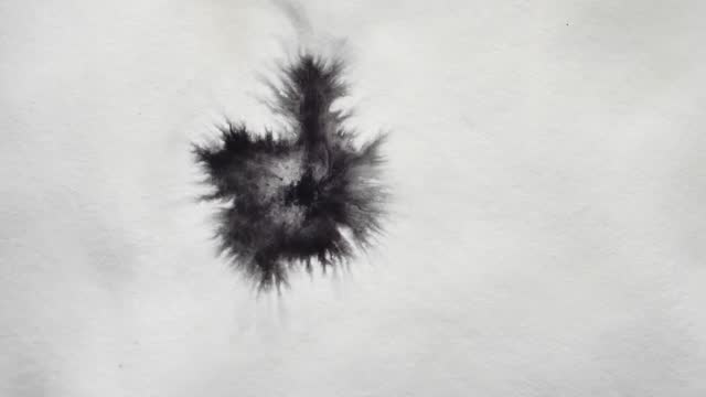 a drop of black paint falls on the white surface and spreads over it