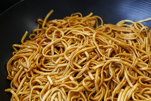 Close up Asian stir fried egg noodles with soy sauce in wok pan, high angle view