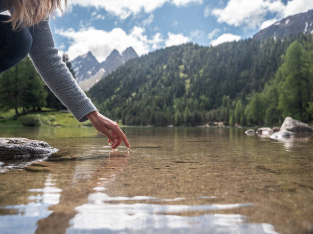 istock Woman's hand touches surface of alpine lake 1301278272