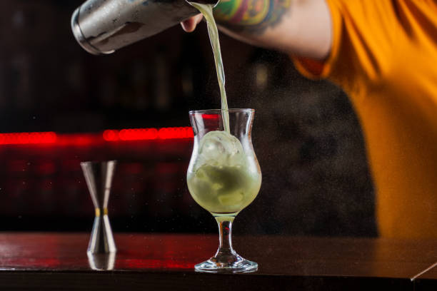 istock Bartender sprinkles on illuminated glass with bright green cold cocktail on bar counter and makes fire flame over it. 1301279291