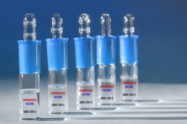 istock Blue glass ampoules flask with vaccine on blue backdrop with hard shadows. Dose of a possible coronavirus vaccine. 1301283036