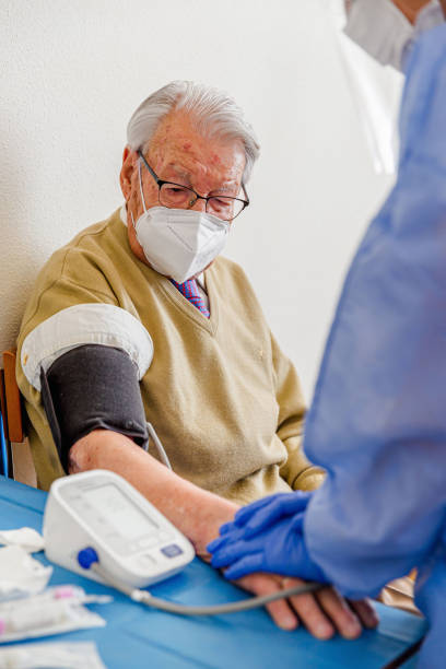 pielęgniarka z maską biorąc ciśnienie krwi starszego mężczyzny - senior adult 80 plus years aging process clothing zdjęcia i obrazy z banku zdjęć