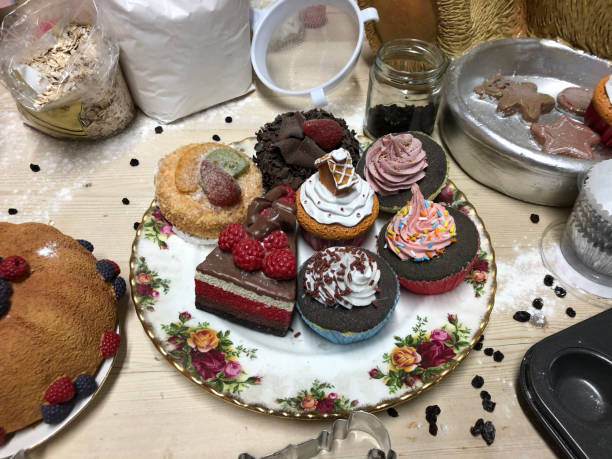 istock Image of wooden table top Christmas baking display, artificial, plastic cakes on bone china plate, flour bag, oats, sieve, muffin tin, focus on foreground 1301287297