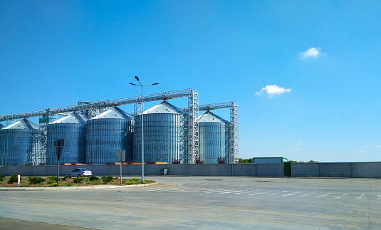 Modern granary, grain drying complex, covered elevators on the farm in the field, agriculture. Against the blue sky