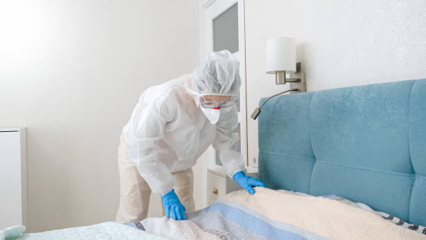 Young housewife in protective biohazard suit making up bed during covid-19 pandemic and lockdown stock photo