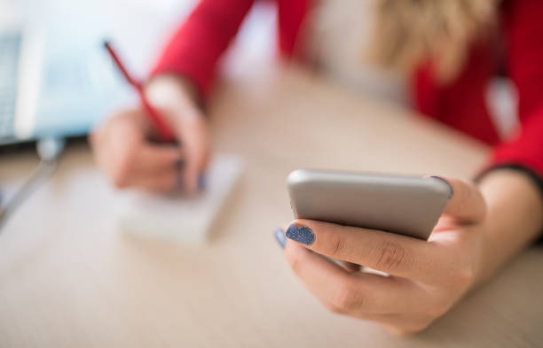 istock Close up of a woman holding smartphone and writing notes 1301292802