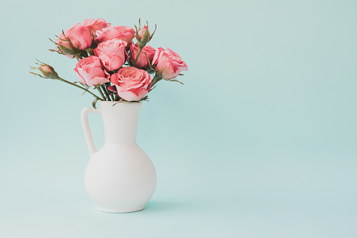 Bouquet of pink roses in white vase on light blue background. Copy space