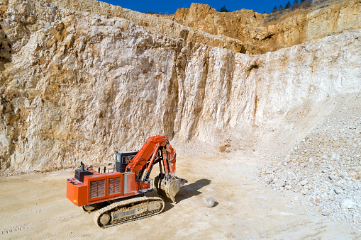 Heavy, orange excavation machine in a quarry from above.