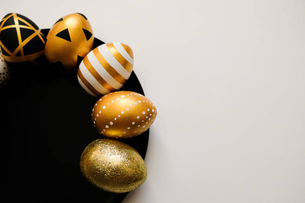 istock Stylish Easter golden decorated eggs on black plate isolated on white background. Trendy flat lay easter. Happy Easter card with copy space for text. Minimal easter concept 1301302224
