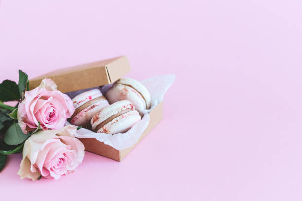 Tasty french macaroons in a box with pink roses on a pink pastel background. Tasty french macaroons in a box with pink roses on a pink pastel background. Place for text. bud candy stock pictures, royalty-free photos & images
