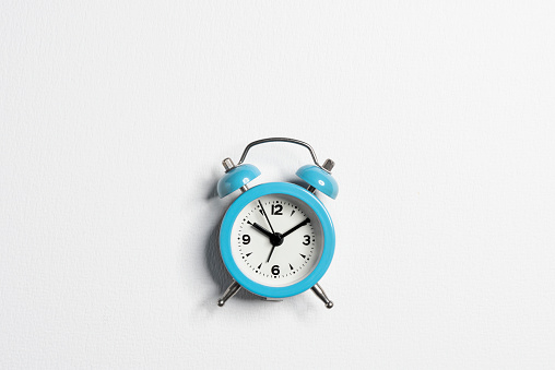 Alarm clock in blue case shows 10 past 10 o'clock. Front view isolated on white with copy space