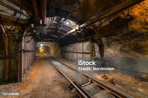 istock Tunnel of the mining of an underground mine. Lots of pipelines on the ceiling and rail track for trolleys 1301318485
