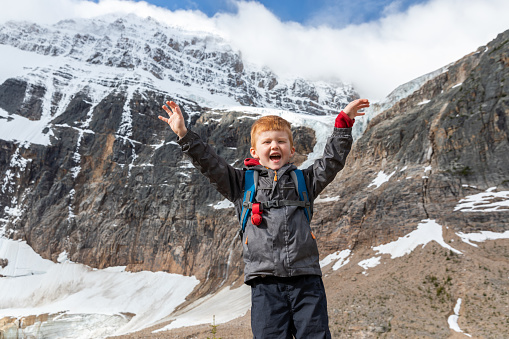 The emotion of joy of a little boy climbing on a pile of large stones, the child shouts.