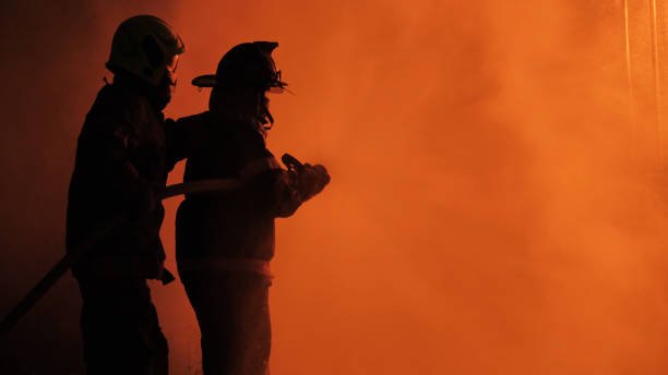 Firefighter spray water fighting Rear view of Asian fireman wear fire protection suit. Firefighter spray water fighting. Emergency, Fire! at night extinguishing stock pictures, royalty-free photos & images