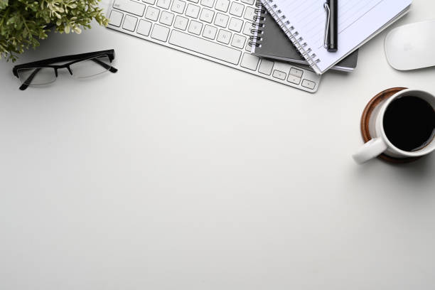 istock Top view of white office desk with notebook, wireless keyboard, coffee cup, glasses and copy space. 1301325606