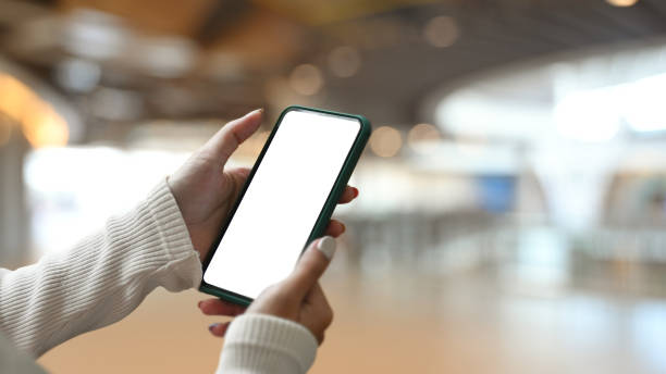 istock Close up view of young woman holding smart phone with empty screen on shopping mall blurred background. 1301325607
