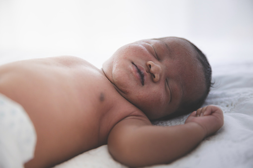 Close up of Mixed race black boy Ethnicity Thai-Nigeria. Newborn baby sleeping on the bed in home and nature sunlight