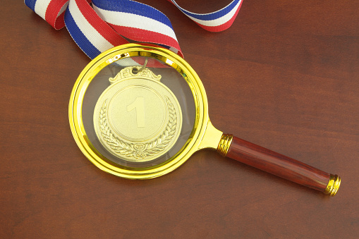 Investigate result of competition concept. Gold medal and magnifying glass.