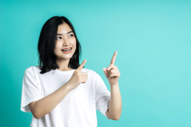 istock Young elegant Asian woman smiling and pointing to empty copy space isolated on blue background 1301334638