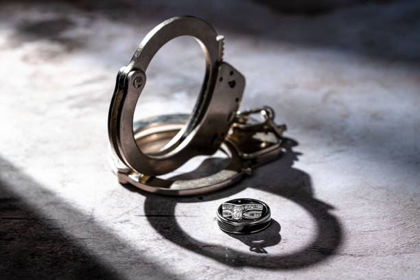 Handcuffs in Shadow Light with Diamond Wedding Rings and possible Jail for Domestic Violence Divorce or Marriage Trouble Concept with handcuffs and diamond wedding rings in dark contrast light independence document agreement contract stock pictures, royalty-free photos & images