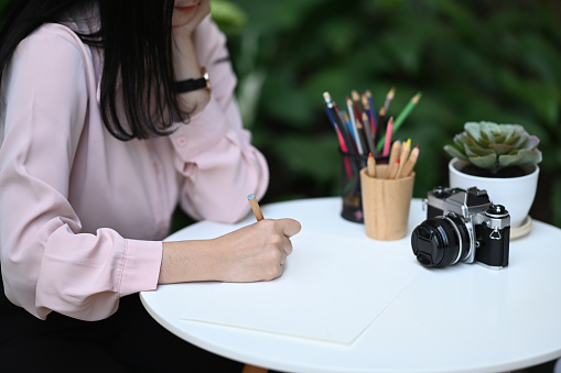 Cropped shot of young female freelance sitting at outdoor and making note on empty notebook.