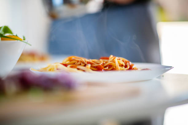 Plate of boiled spaghetti with steaming hot Bolognese sauce on the table