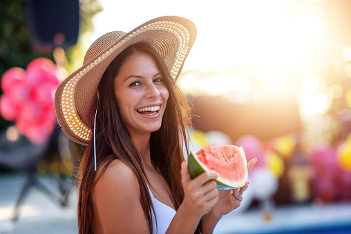 Happy young woman eating watermelon by the swimming pool. Happiness, people, holiday and summer concept.