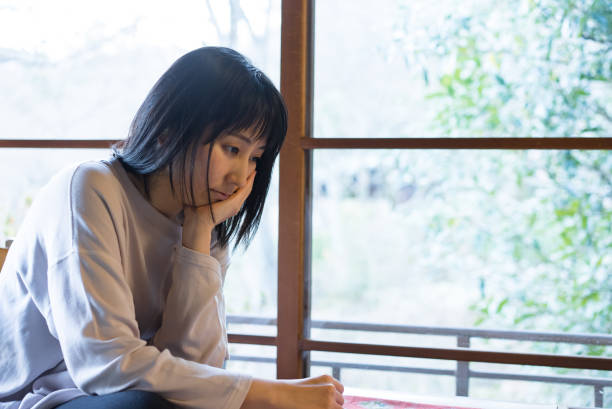 Portrait of an Asian woman at a window Portrait of an Asian woman at a window.

Model: Japanese.
Inside a Japanese house.
Pondering.
Relaxation wear, lounge wear, pajamas, long sleeves. window seat vehicle stock pictures, royalty-free photos & images
