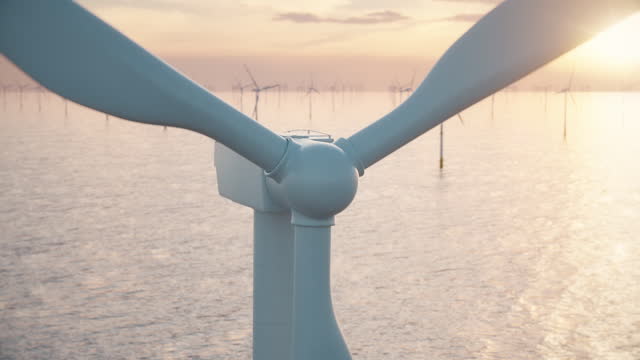 Close-up of a wind turbine and a wind park in the sea against low sun